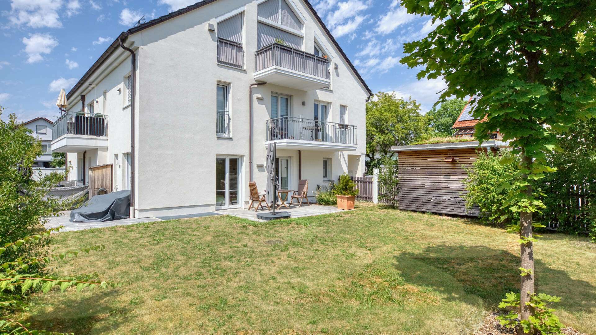 Rear view of the white-plastered residential building of the garden apartment in Munich-Lerchenau with balconies and garden