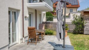 Terrace of the garden apartment in Munich-Lerchenau with wooden chairs, sun umbrella and view of the garden