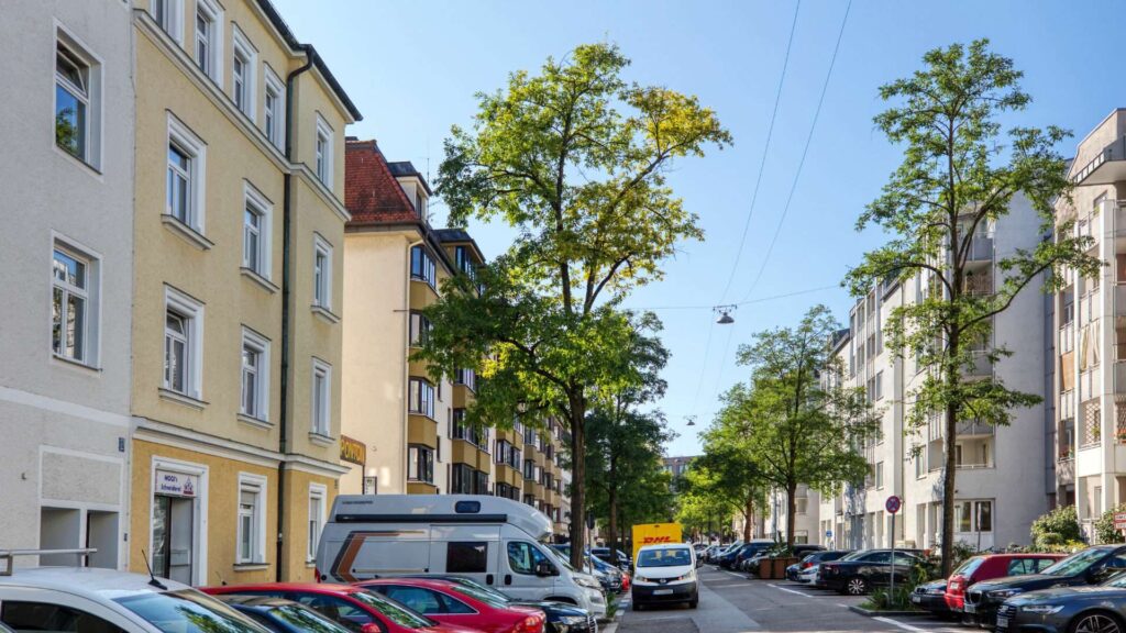 Baumbestandene Straße mit Altbaufassaden und parkenden Autos in der Ludwigsvorstadt.