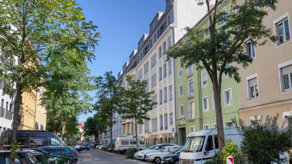 Altbaustraße in der Ludwigsvorstadt mit bunten Fassaden, Bäumen und parkenden Fahrzeugen.