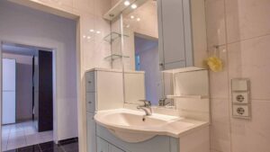 Badezimmer in Maxvorstadt mit blau-grauem Waschtisch, Spiegel mit Glasablagen und cremefarbenen Wandfliesen.