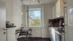 Helle Küche in Maxvorstadt mit dunkler Arbeitsplatte, rundem Esstisch, schwarzen Stühlen und Kaffeemaschine am Fenster.