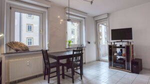 Möbliertes Wohnzimmer mit Esstisch, Fernseher und zwei Fenstern in der Wohnung in München-Maxvorstadt