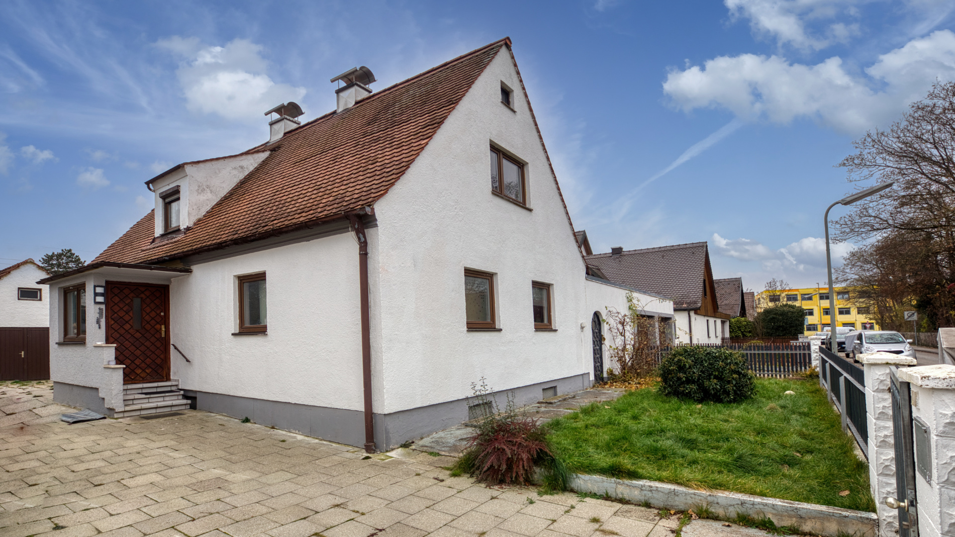 Weißes Einfamilienhaus mit rotem Satteldach und gepflasterter Einfahrt in München-Milbertshofen.