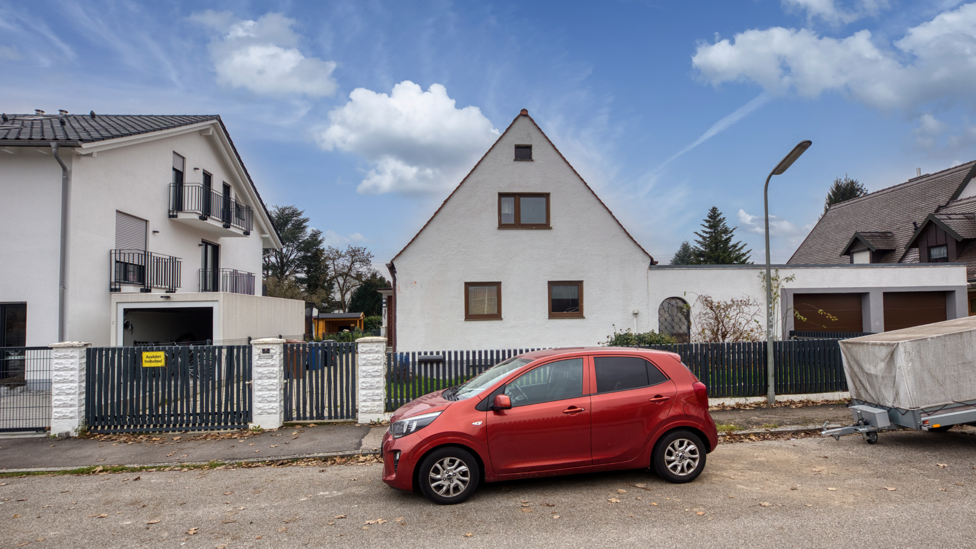 Grundstück in Milbertshofen mit weißem Mehrfamilienhaus, giebelständigem Haus und rotem Kleinwagen.