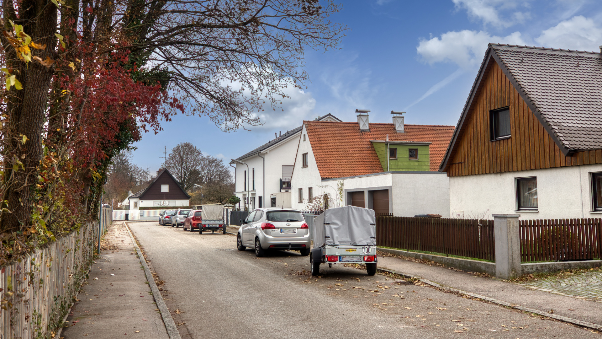 Schmale Dorfstraße mit historischen Häusern und parkenden Autos im Stadtteil Milbertshofen in München