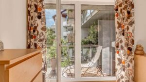 Balcony door with patterned curtain and a view of the greenery in an apartment in Munich-Milbertshofen