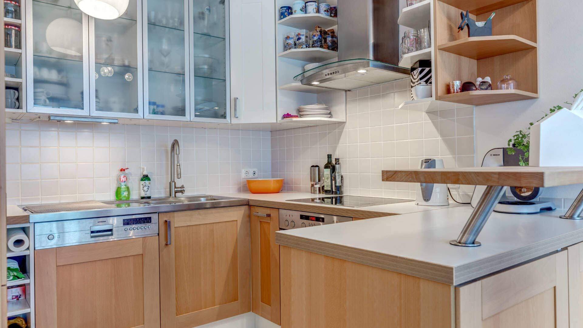 Kitchen in the apartment in Milbertshofen with wooden fronts, glass cabinets, extractor hood and worktop