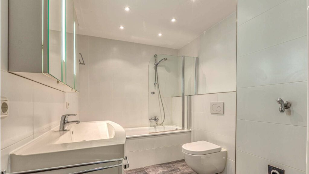 Modernes Badezimmer in Moosach mit Badewanne, Dusche, beleuchtetem Spiegel und freistehendem WC.