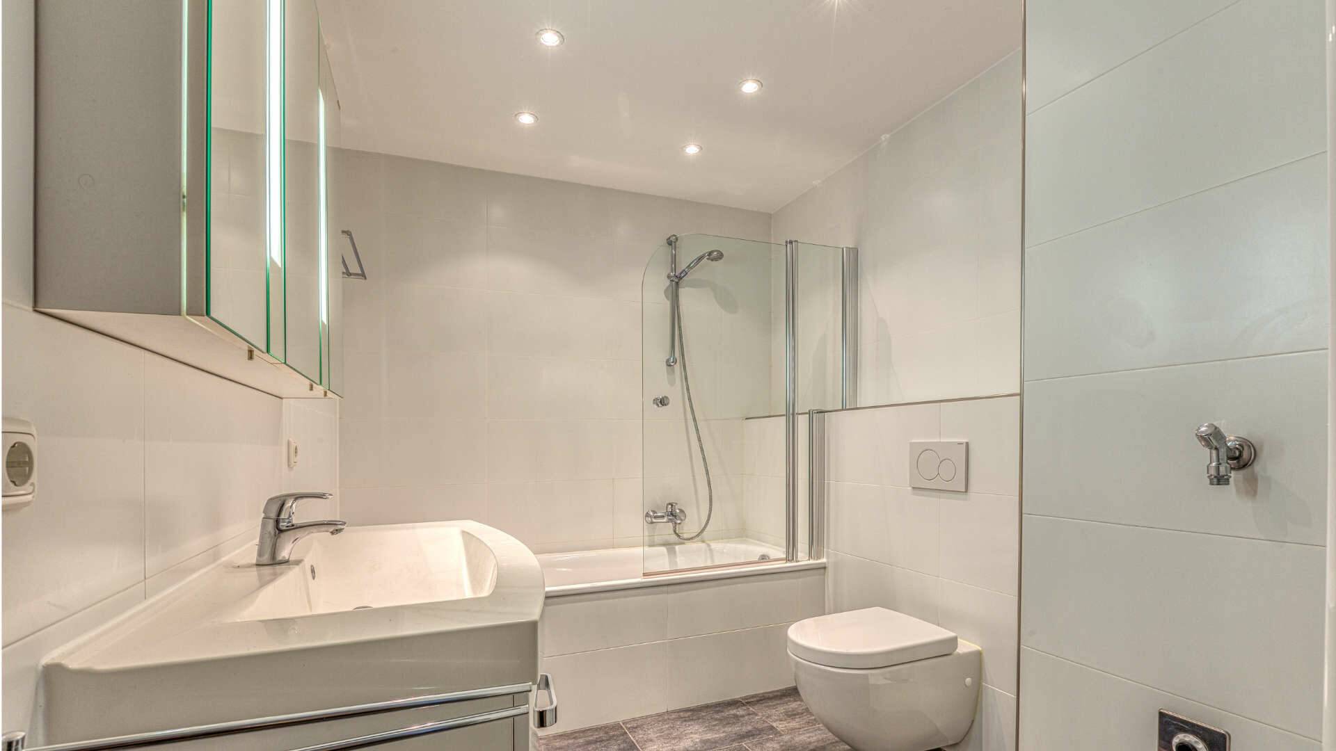 Modern bathroom in Moosach with bathtub, shower, illuminated mirror and a separate toilet.