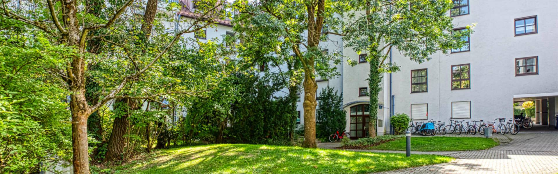 Residential building in Moosach with a white facade, surrounded by large trees and a well-kept green area.