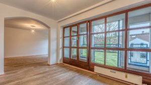 Empty living room in Moosach with large bay windows, parquet floor and a view into an adjoining room.