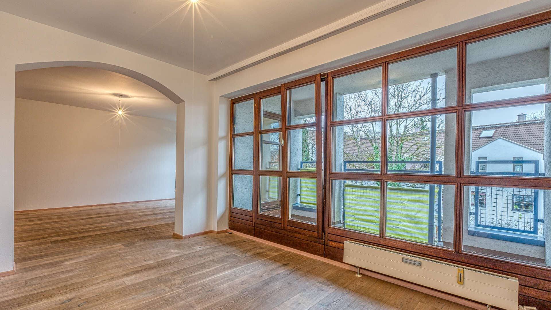 Empty living room in Moosach with large bay windows, parquet floor and a view into an adjoining room.