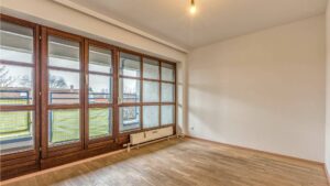 Empty living room with a continuous window front and garden view in the apartment in Munich-Moosach