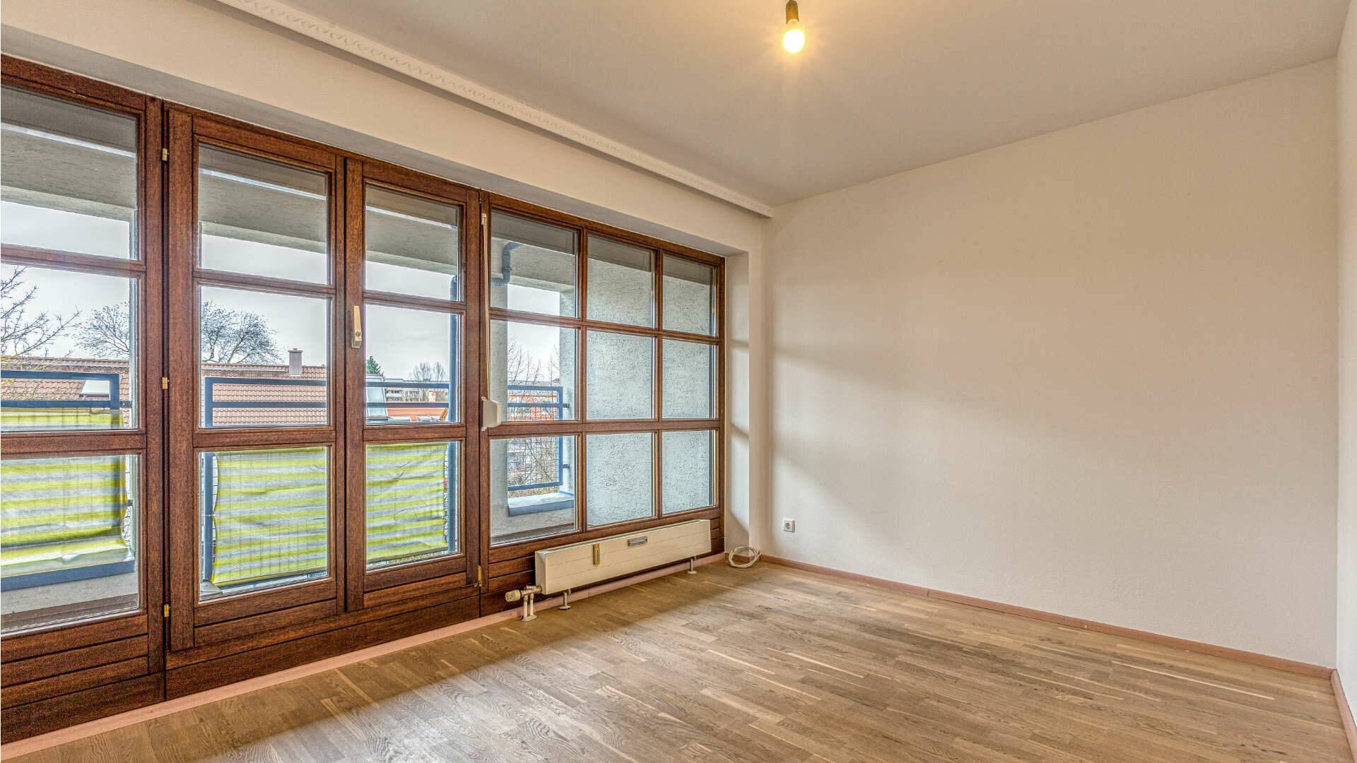 Empty living room with a continuous window front and garden view in the apartment in Munich-Moosach