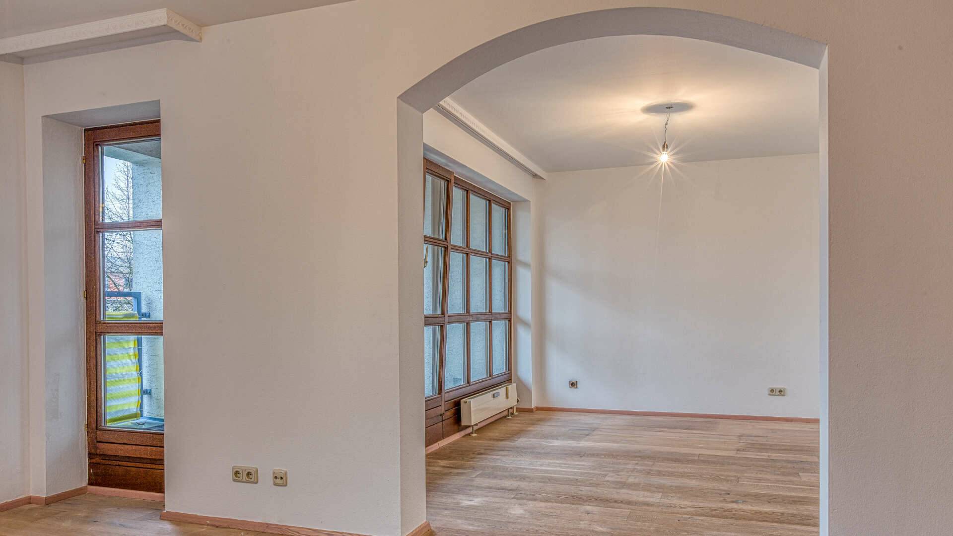 Empty room with a balcony window and light parquet floor in the hallway of the apartment in Munich-Moosach
