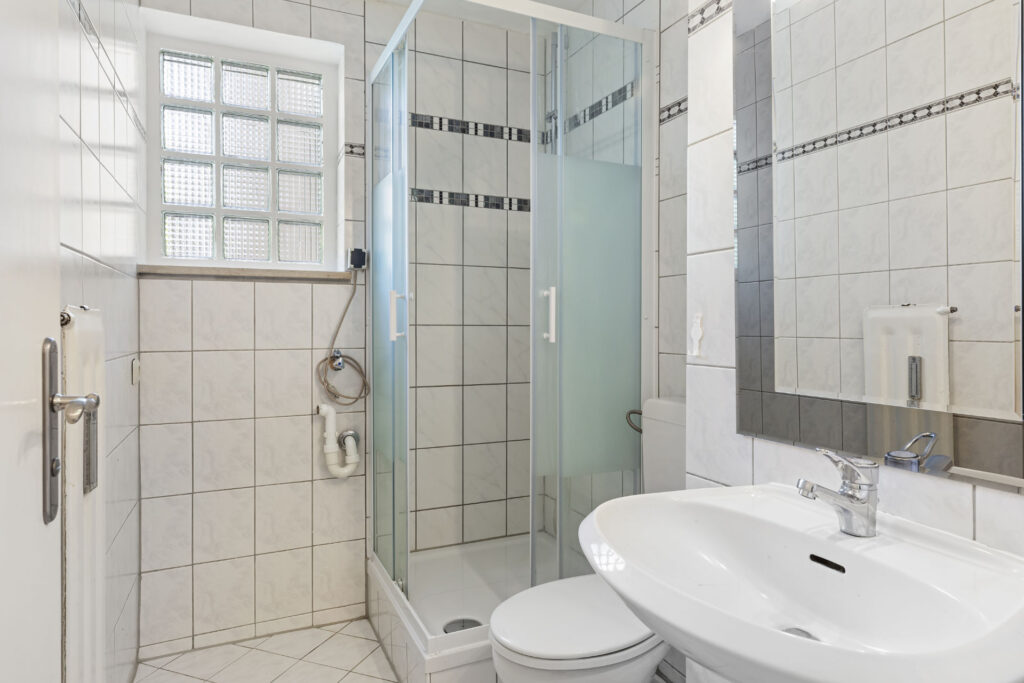 Simple bathroom in Fürstenried-West with shower, toilet, sink and tiles.
