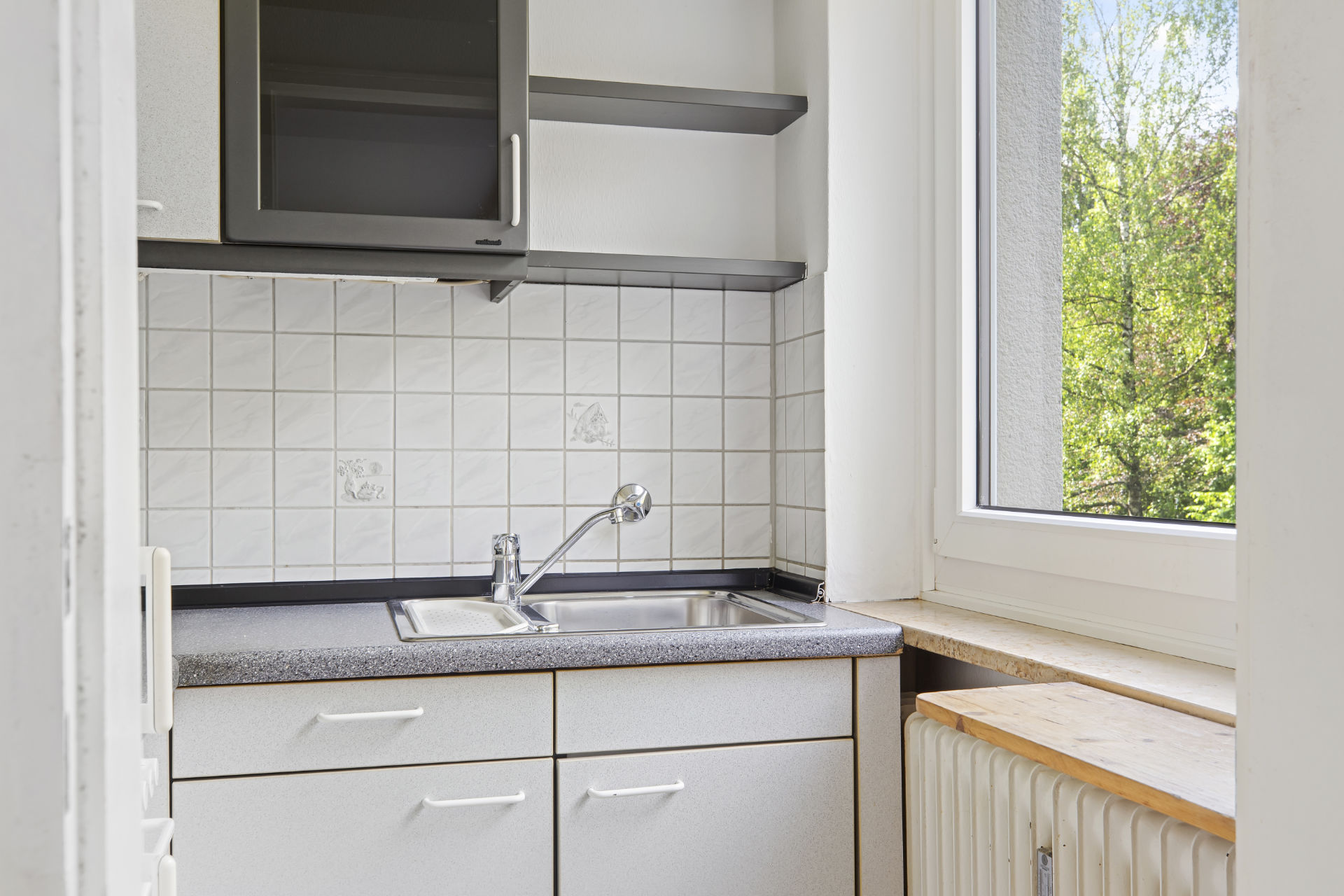 Small kitchen in Fürstenried-West with white cabinets, sink, and window with a view of greenery.