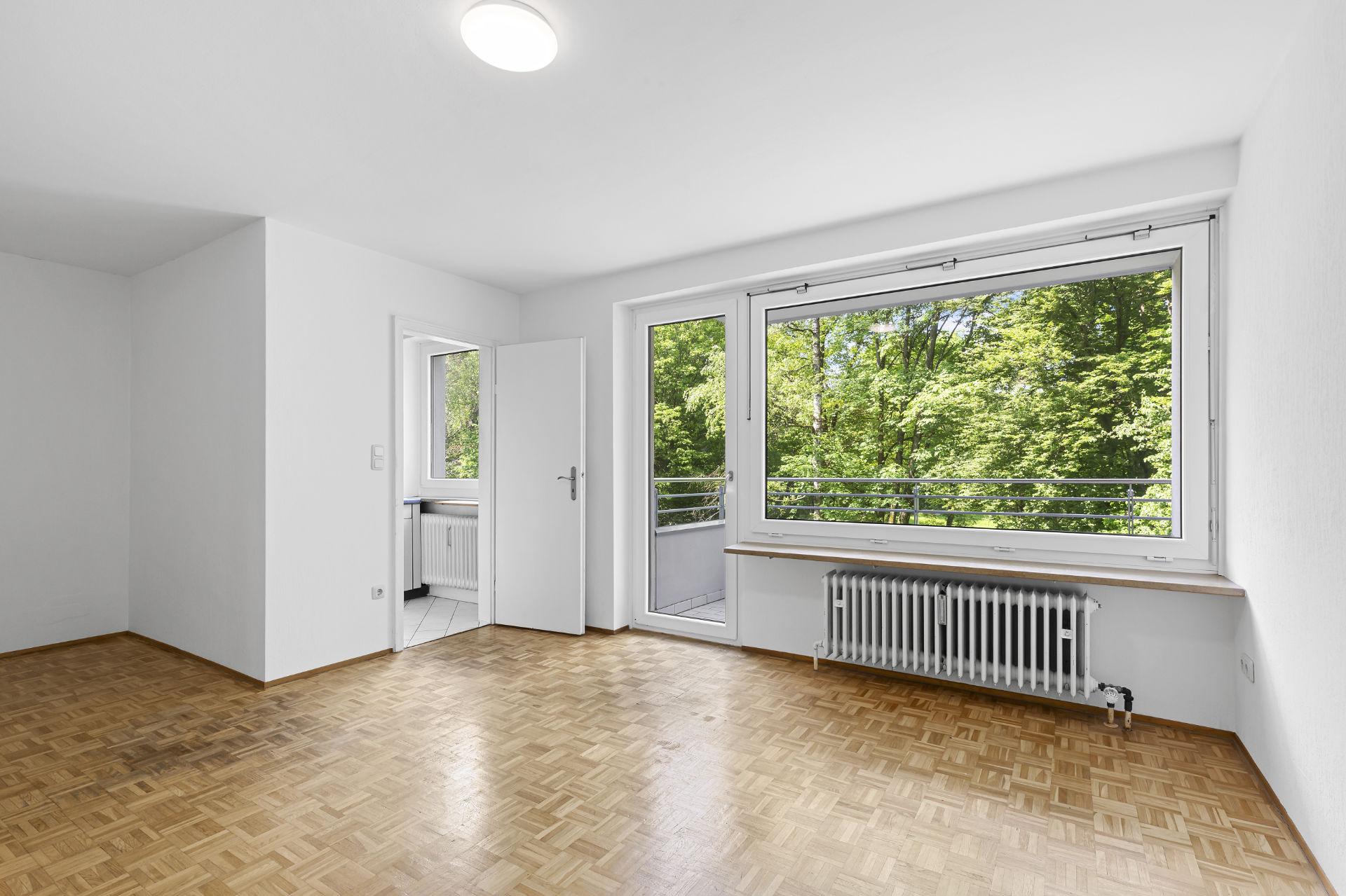 Empty room in Fürstenried-West with parquet flooring, large window, and balcony access.