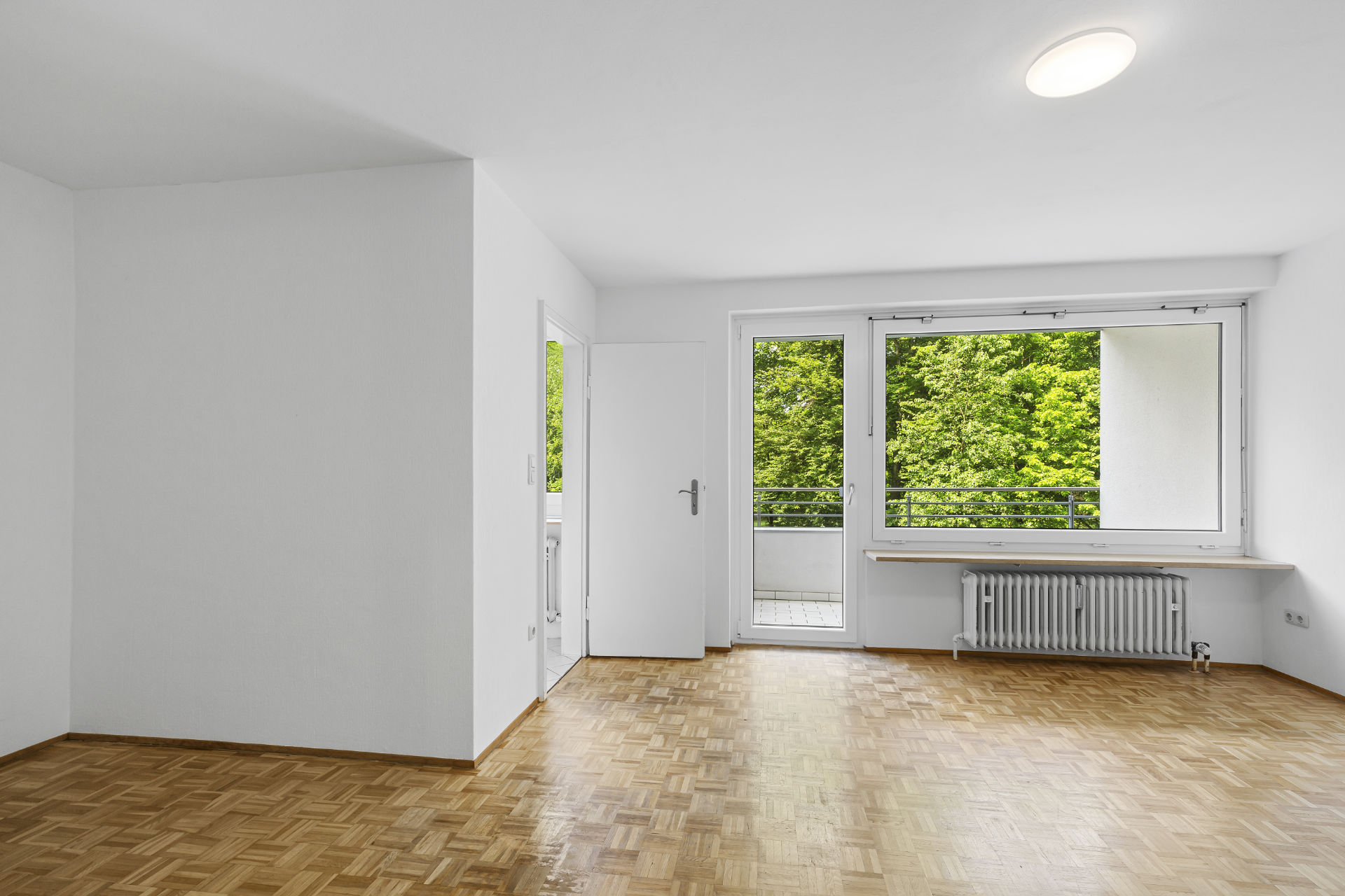 Unfurnished room with parquet flooring and balcony door with a green view in an apartment in Munich-Fürstenried-West