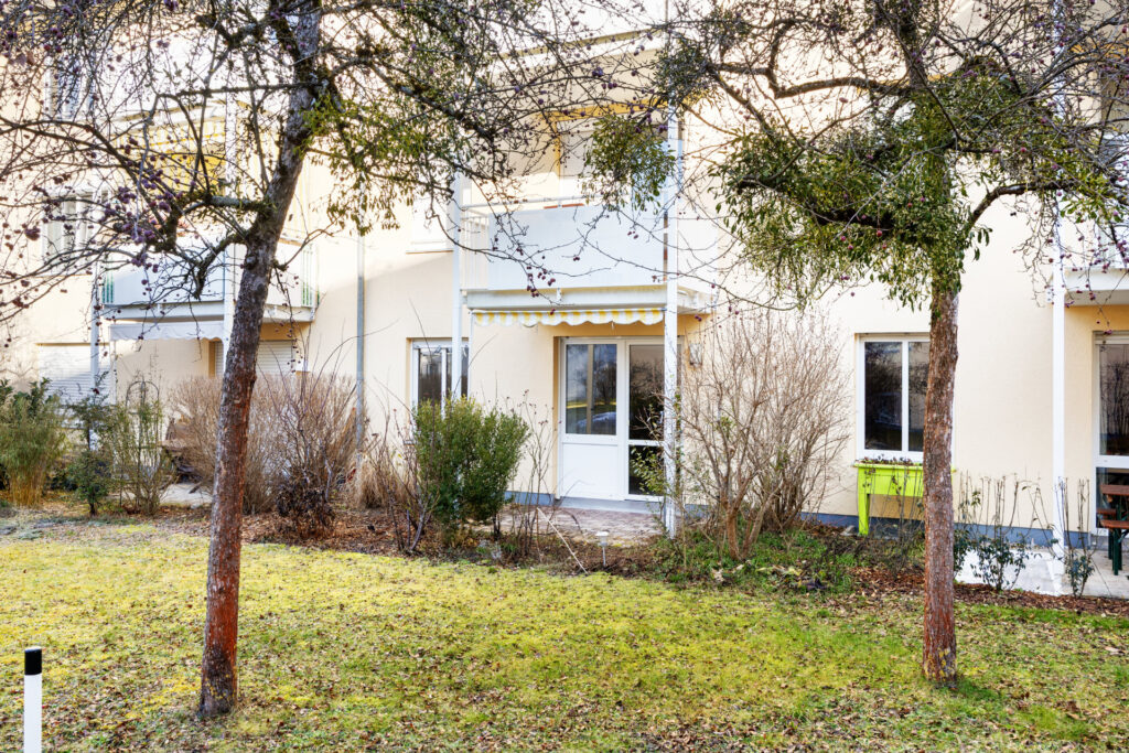 Yellow house façade of the Großhadern residential complex with balconies, patio door, and a winter garden