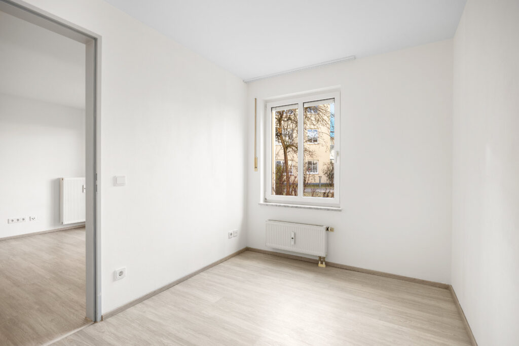 Empty bedroom of the apartment in Großhadern with light laminate flooring and a window facing the inner courtyard