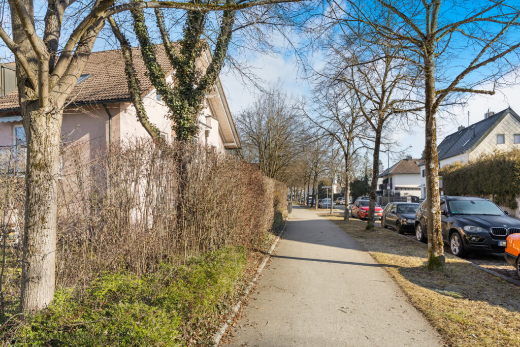 Sidewalk with hedge, trees, and parked cars in the neighborhood of the apartment in Großhadern