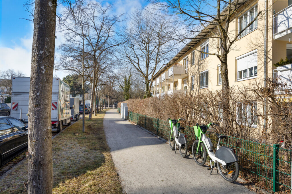 Sidewalk in front of apartment building in Großhadern with e-bike rental station and hedge in the neighborhood of the apartment