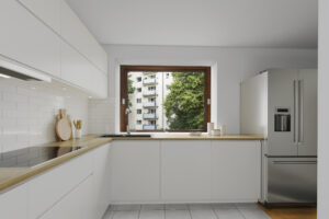Virtual rendering of a white kitchen with window, refrigerator, and view of trees in Munich-Lehel