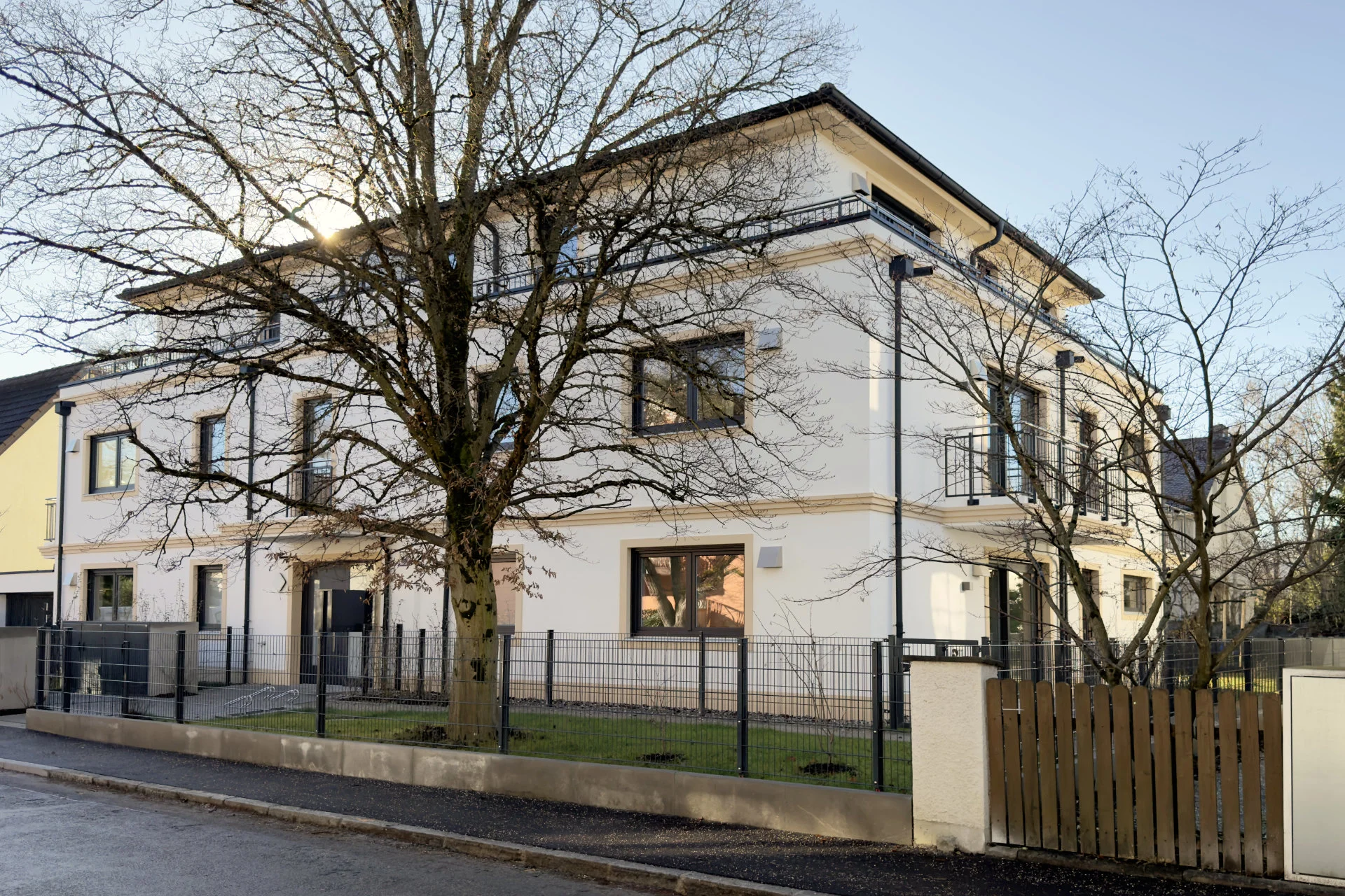 Street view of the white residential building with a large tree in Munich-Pasing at dusk