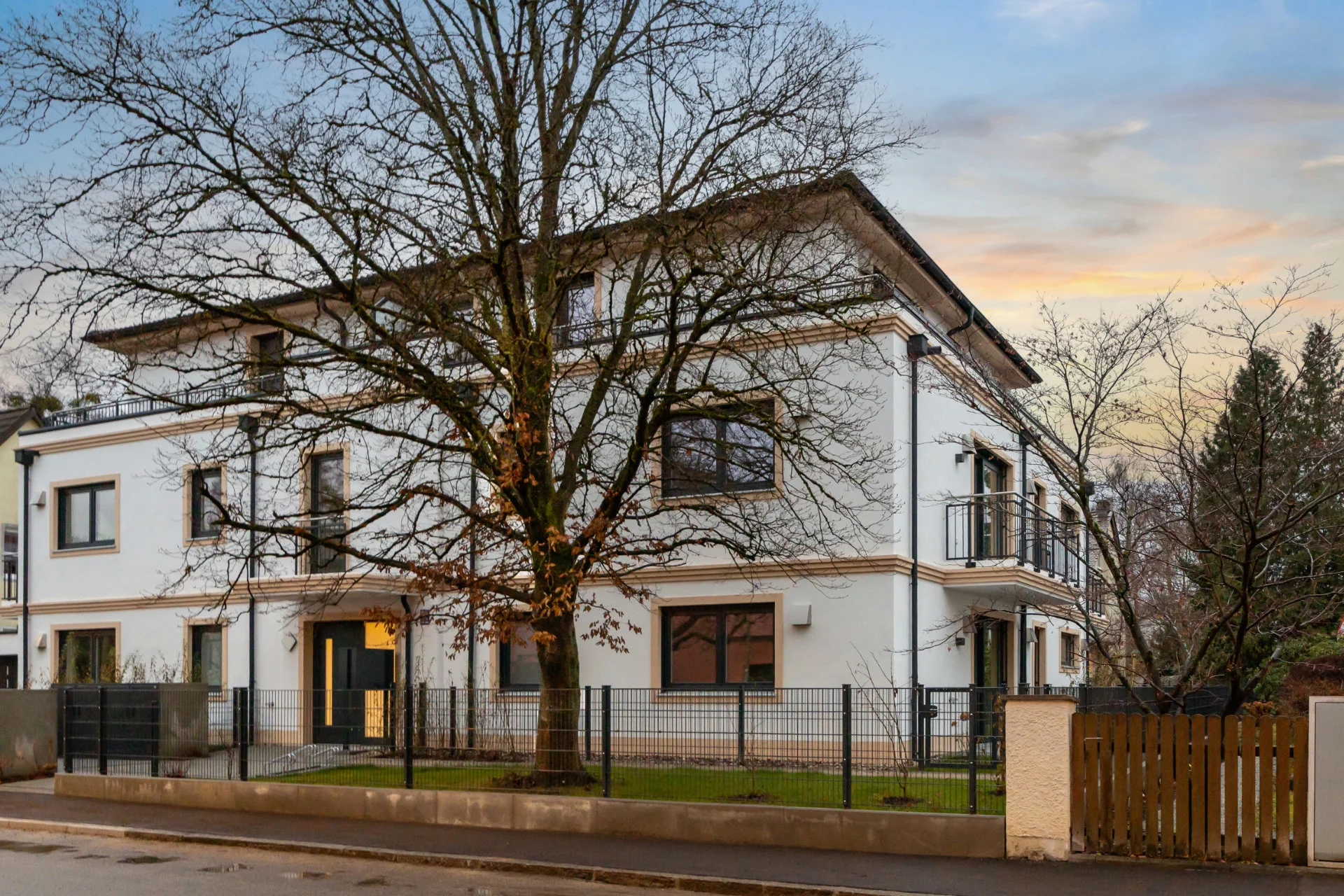 White apartment building with a large tree in front in Munich-Pasing at dusk