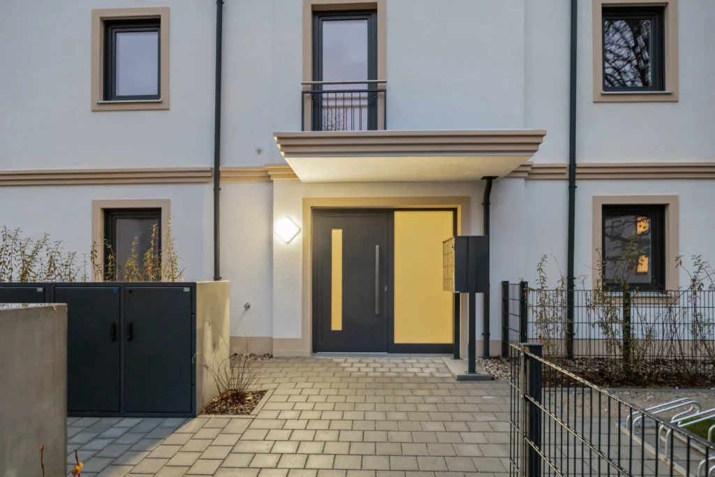 Entrance to the apartment building with a yellow front door and canopy in Munich-Pasing in the evening