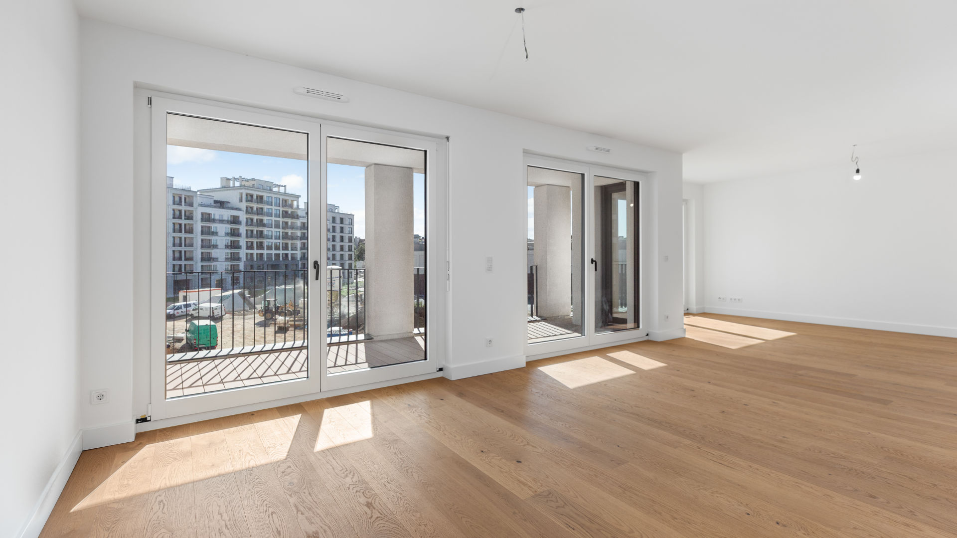 Unmöblierter Wohnraum einer Neubauwohnung mit Balkonzugang und Parkettboden in München