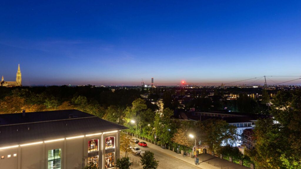Abendlicher Ausblick mit beleuchtetem Kirchturm und Stadtsilhouette vom Nockherberg