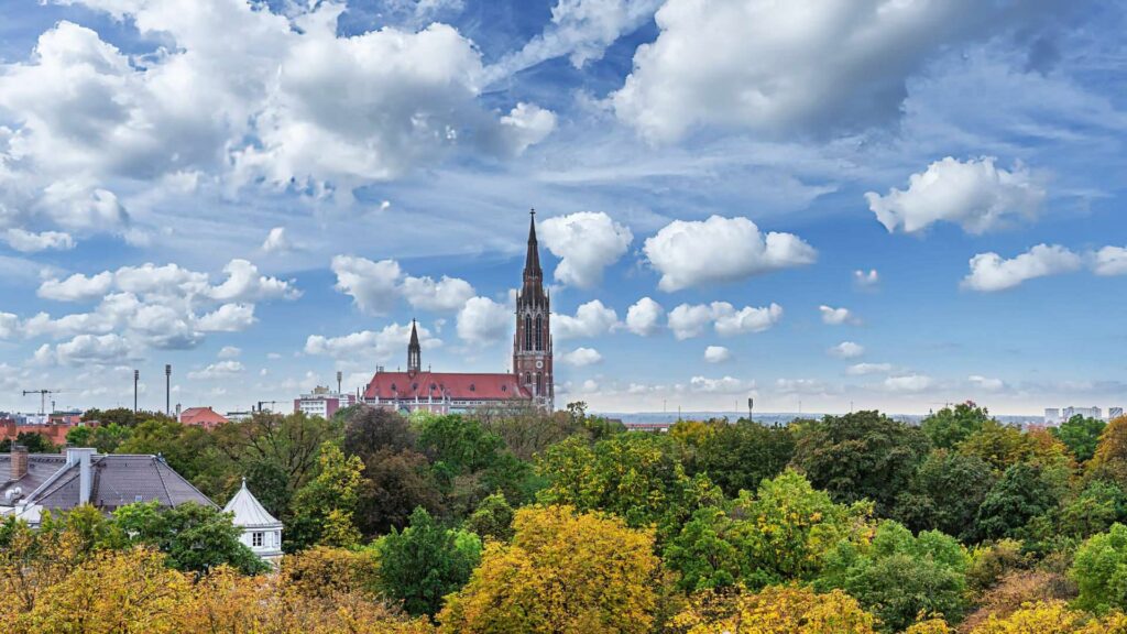 Blick auf einen Kirchturm hinter herbstlich gefärbten Bäumen vom Nockherberg aus