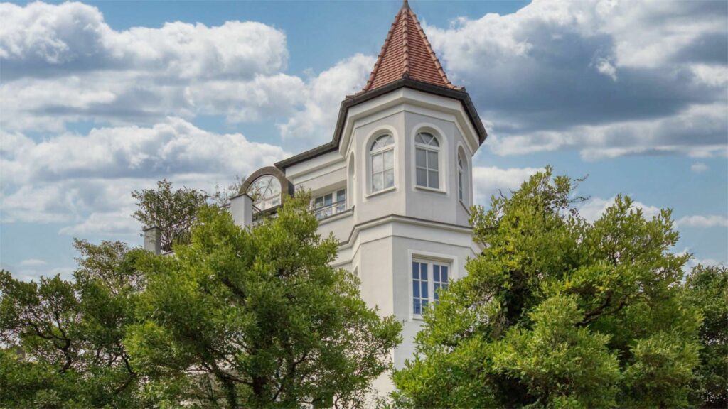 Tower villa with a red pointy roof surrounded by tree tops in Nymphenburg