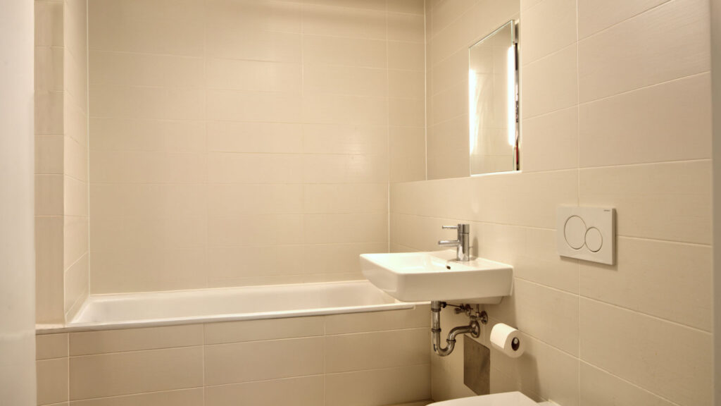 Modern bathroom with bathtub, washbasin, and illuminated mirrored cabinet in an apartment in Munich-Obergiesing