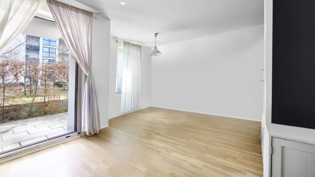 Unfurnished living room with light parquet flooring and patio door in an apartment in Munich-Obergiesing