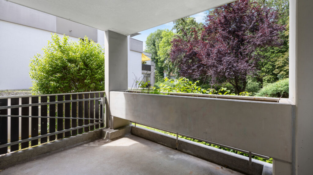 Covered balcony with concrete railings and views of flowering trees in an apartment in Munich-Pasing