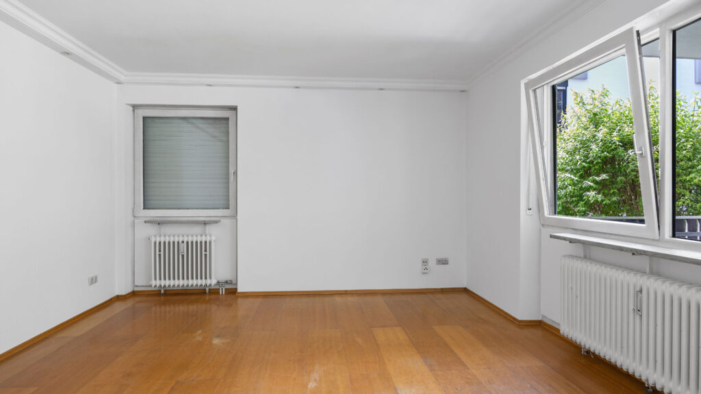 Unfurnished living room with parquet floor and corner window with green views in apartment Munich-Pasing