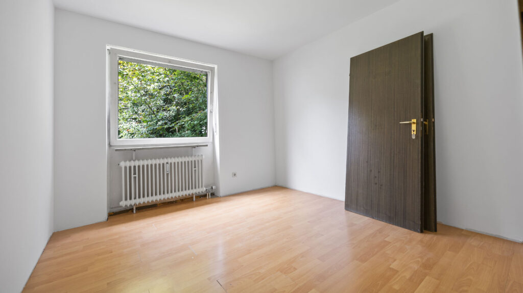 Empty room with light parquet, windows and dark wooden door in Pasing