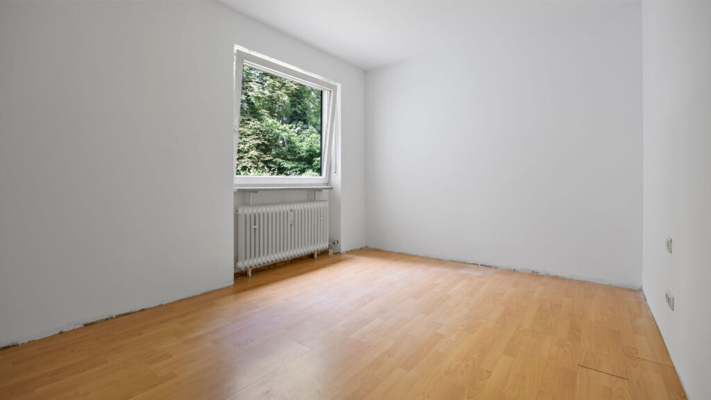 Empty room with parquet floor and windows with greenery in Pasing