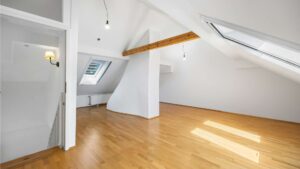 Empty attic room with sloping ceiling, skylight, and light parquet flooring in Planegg