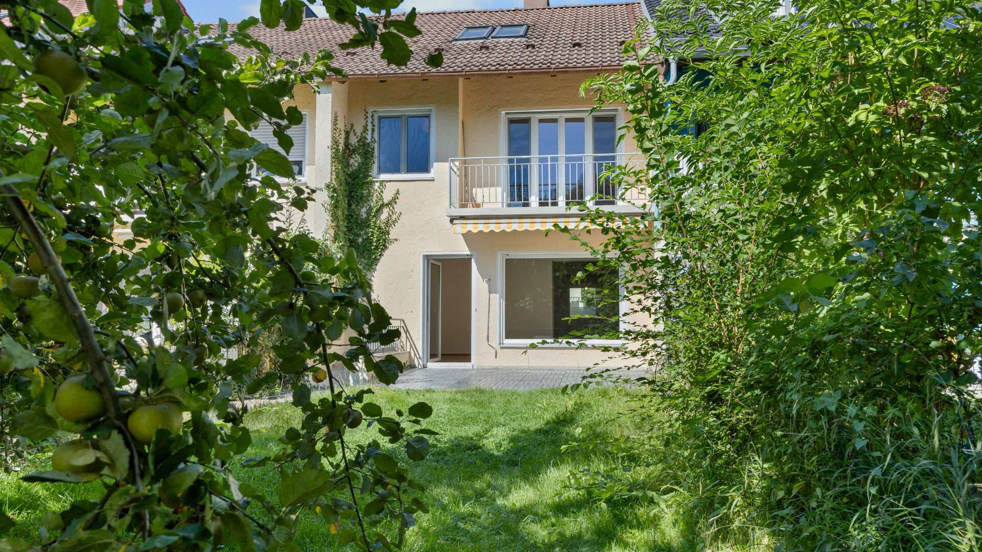 Rear view of the house with balcony, framed by fruit tree branches in the Planegg garden