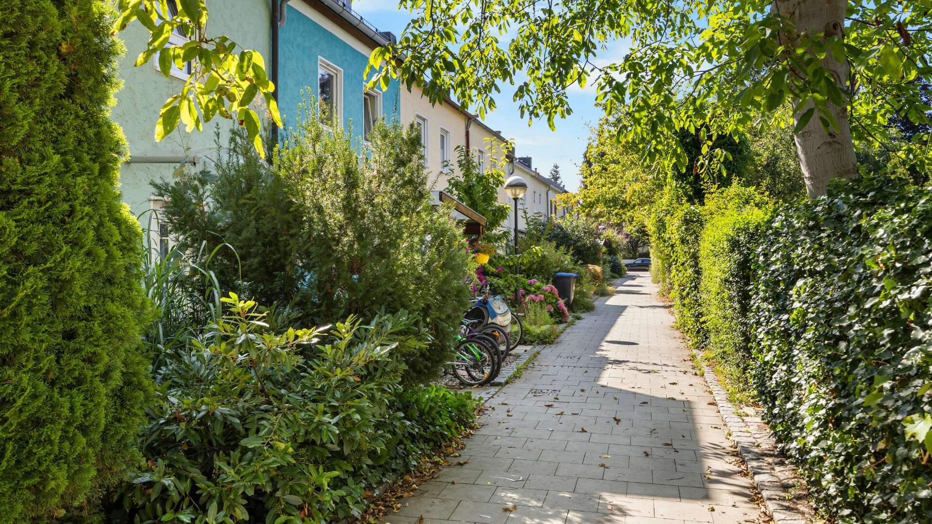 Green footpath with a child on a bicycle between terraced houses in Planegg