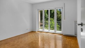 Empty room with parquet flooring and balcony door to the garden in the Planegg house