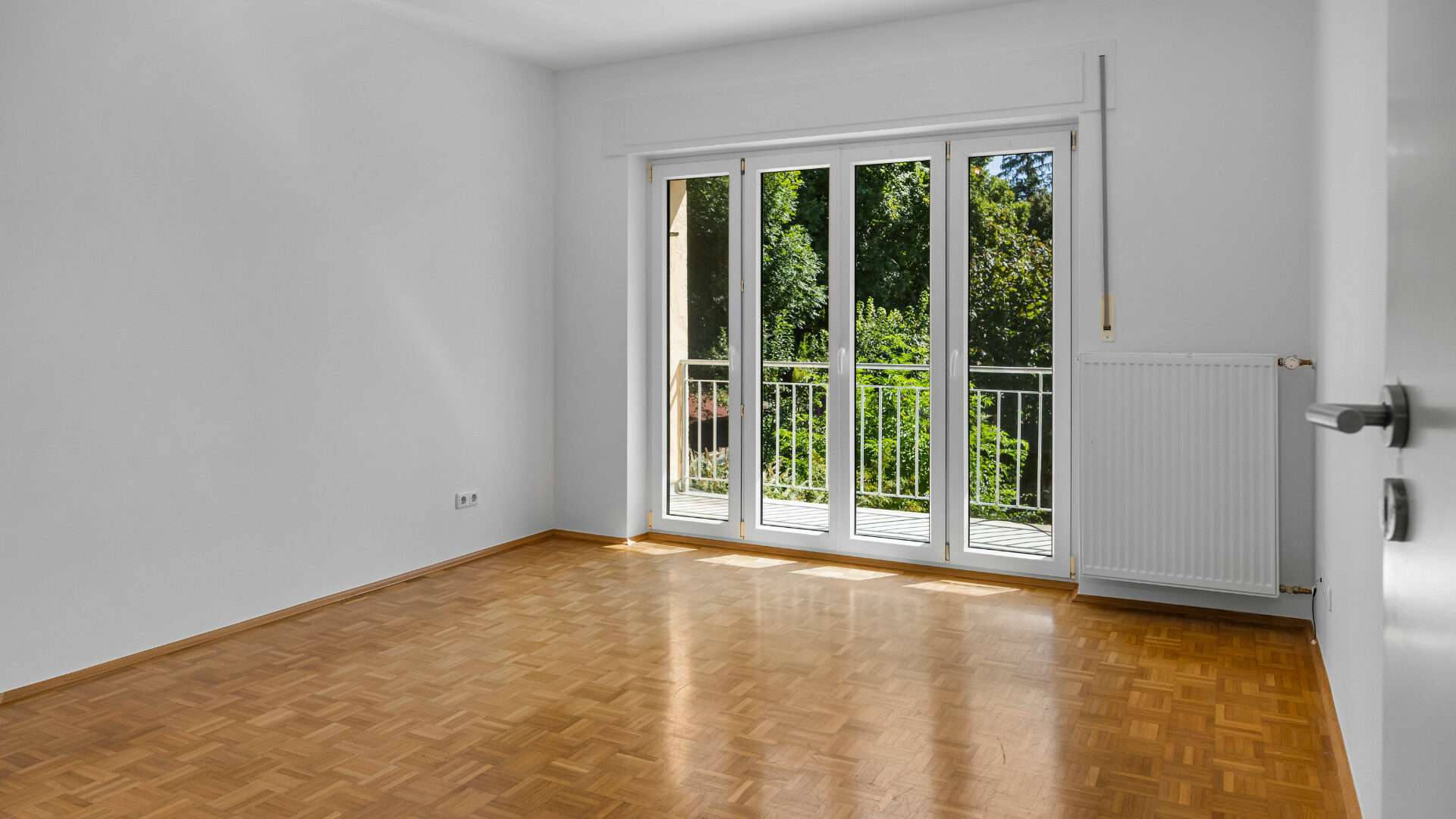 Empty room with parquet flooring and balcony door to the garden in the Planegg house