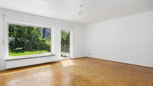 Empty living room with large front window, parquet flooring and view of the garden, Planegg