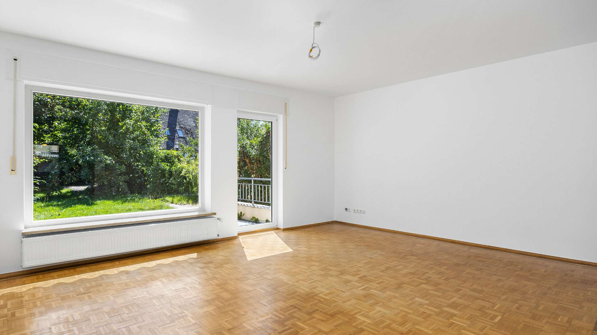 Empty living room with large front window and parquet flooring in the Planegg townhouse