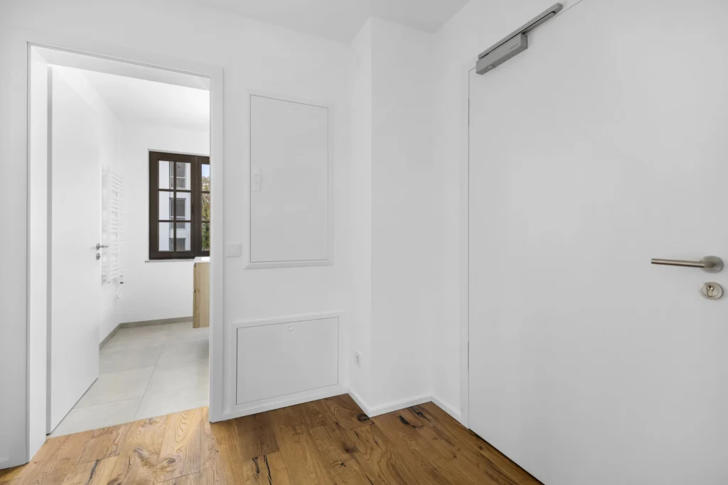 Bright hallway with wooden floor and view into the bathroom of the rental apartment in Pöcking